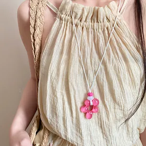 Primo piano di una collana con ciondolo a fiore in resina rosa su un top beige a pieghe