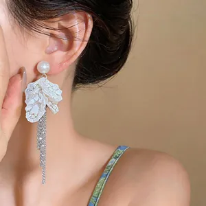 Detail shot of elegant white petal tassel earrings with pearls on an Asian model.