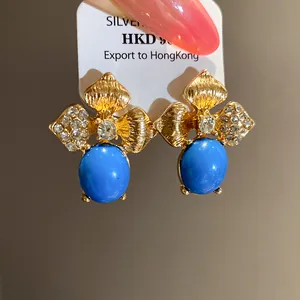 Detailed view of vintage gold leaf earrings featuring blue enamel stones and sparkling rhinestones