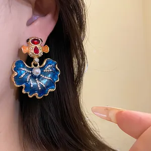 Macro view of vintage blue enamel leaf earring with red stones and crystals on ear.