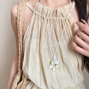 Dettaglio di un ciondolo a fiore in resina su una collana di corda bianca indossata da una modella