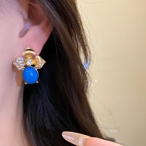 Close-up of vintage gold leaf stud earring featuring a vibrant blue stone and crystal accents
