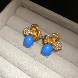 Macro view of vintage gold leaf stud earrings with blue oval stone and rhinestones