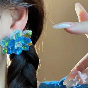 Détail rapproché de boucles d'oreilles fleurs en verre bleu portées par un mannequin