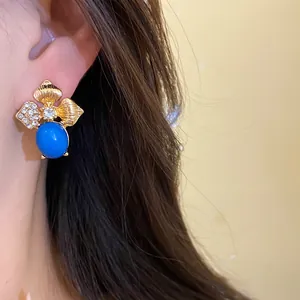 Close-up view of vintage gold leaf earrings featuring a blue stone and rhinestones on ear