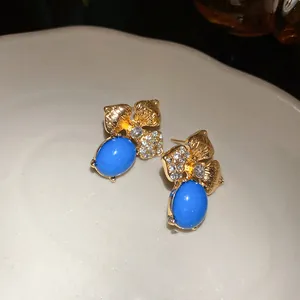 Detailed view of vintage gold-tone leaf earrings with blue enamel and sparkling rhinestones.