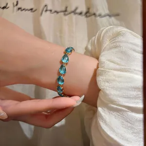 Close-up detail of an elegant gold bracelet featuring teardrop-shaped blue zircon stones.