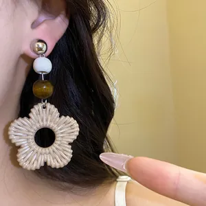 Close-up detail of large beige resin flower drop earring with wooden beads on ear