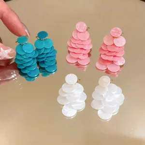 Dettaglio di orecchini a bottone in acrilico marmorizzato in blu, rosa e bianco.