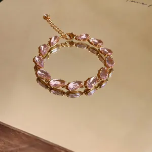 Close-up of pink pear-cut zirconia bracelet reflecting on a gold mirror surface