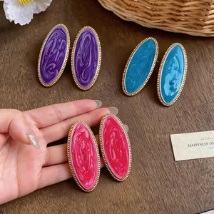 Nahaufnahme von ovalen Emaille-Ohrringen in Violett, Blau und Rosenrot auf Holzoberfläche