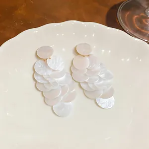 Macro di orecchini a nappa in acrilico cangiante su un piatto di ceramica bianco.