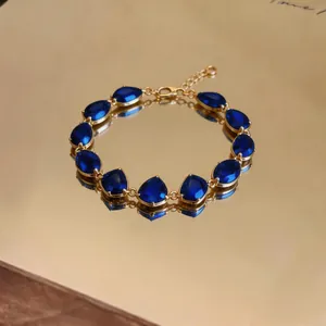 Close-up detail of an elegant gold bracelet with blue teardrop-shaped zircon stones
