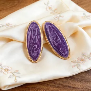 Nahaufnahme von violetten marmorierten ovalen Ohrringen mit goldenem Perlenrand