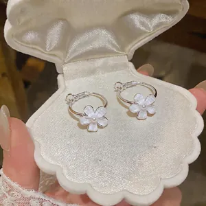 Close-up of elegant silver hoop earrings with white resin flowers in a shell box.