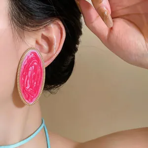 Nahaufnahme von übergroßen rosa marmorierten ovalen Emaille-Ohrringen mit Goldrand