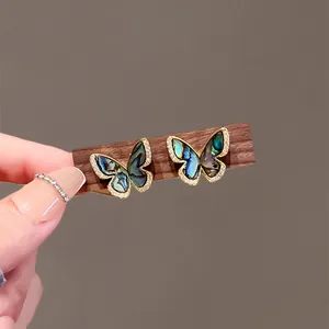 Close-up of butterfly stud earrings with iridescent shell wings and micro-zircon border.