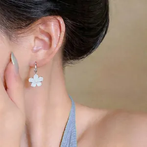Detailed view of elegant silver hoop earrings with white resin flower pendant worn.