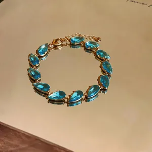 Close-up of gold bracelet with teardrop blue stones on a warm reflective surface