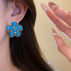 Vintage-style blue resin flower stud earrings with elegant gold trim detail on ear
