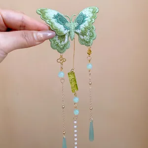 Détail d'une pince à cheveux papillon brodée verte avec d'élégants glands en perles.