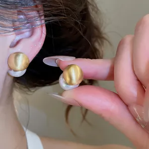 Close-up of matte gold brushed pearl stud earrings with elegant double-sided design
