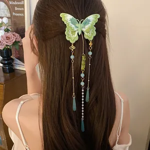 Gros plan d'une pince à cheveux papillon brodée verte avec des glands de perles