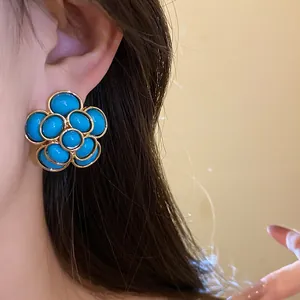 Close-up of vintage resin flower stud earrings with gold trim and blue petals on ear.