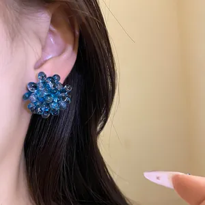 Close-up of deep sea blue beaded flower stud earrings worn on ear showing fine texture