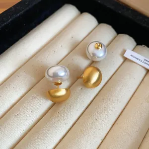 Close-up of elegant double-sided pearl earrings with a brushed gold finish in a velvet box.