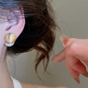 Close-up of elegant brushed gold spherical earrings with pearl detail on ear