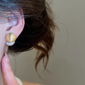 Close-up view of elegant golden brushed metal and white pearl two-way stud earrings on ear