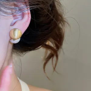 Detailed view of elegant golden brushed round stud earrings with pearl design on model ear