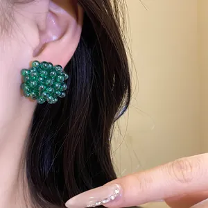 Close-up view of green beaded flower stud earrings worn on ear for detailed product look