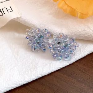 Close-up of blue iridescent beaded flower stud earrings on white textured fabric