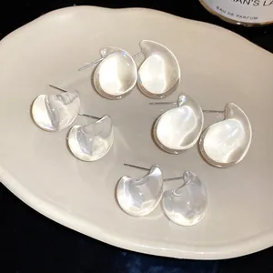 Detailed close-up of transparent acrylic teardrop stud earrings on a beige ceramic tray.