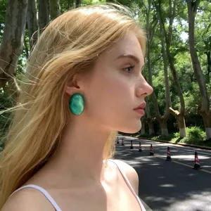 Close-up of a model wearing large French retro green resin stud earrings outdoors.
