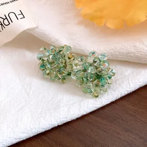 Close-up of cluster bead earrings with teal glass spheres on white fabric background.