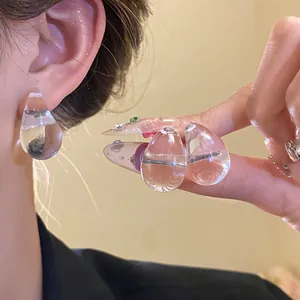 Close-up of minimalist clear acrylic water drop earrings worn showing shiny texture