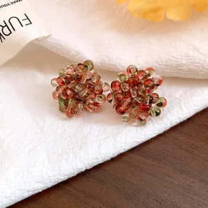 Macro detail view of handmade red and green glass cluster bead earrings on white linen texture