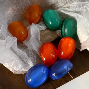 Detailed view of colorful translucent resin stud earrings in orange, green and blue colors