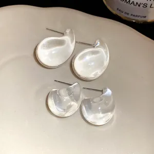 Macro detail of transparent acrylic drop earrings with steel pins on a minimalist ceramic dish