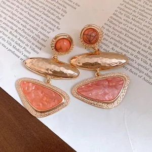 Detailansicht geometrischer Harzohrringe mit gehämmertem Gold-Finish und Korallenakzenten.