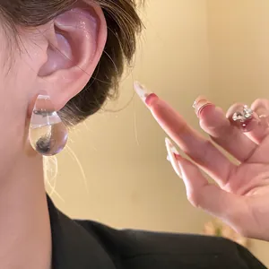 Close-up view showing a stylish transparent acrylic water drop earring worn on the ear