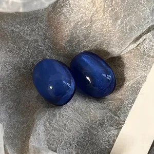 Macro shot of French vintage blue oval resin ear studs with shimmering effect on crinkled paper.
