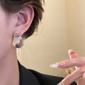 Close-up view of a minimalist clear acrylic water drop stud earring on a model's ear