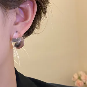 Detail view of a chic clear acrylic teardrop earring with steel needle worn on an ear