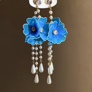 Macro detail of blue mesh flower earrings with white pearl tassels and teardrop pendants.