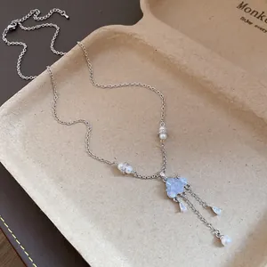 Close-up of silver necklace featuring blue cloud charm and pearl tassel drops