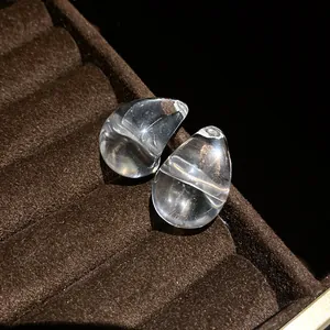 Macro detail of clear acrylic water drop stud earrings displayed on brown velvet jewelry tray
